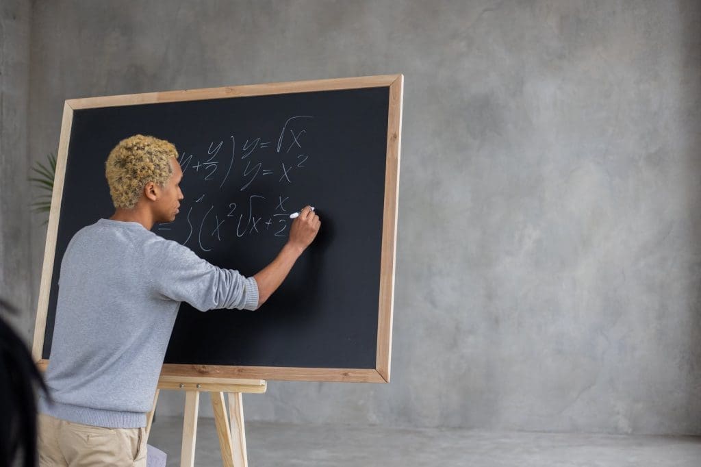 serious black student writing mathematical example on blackboard